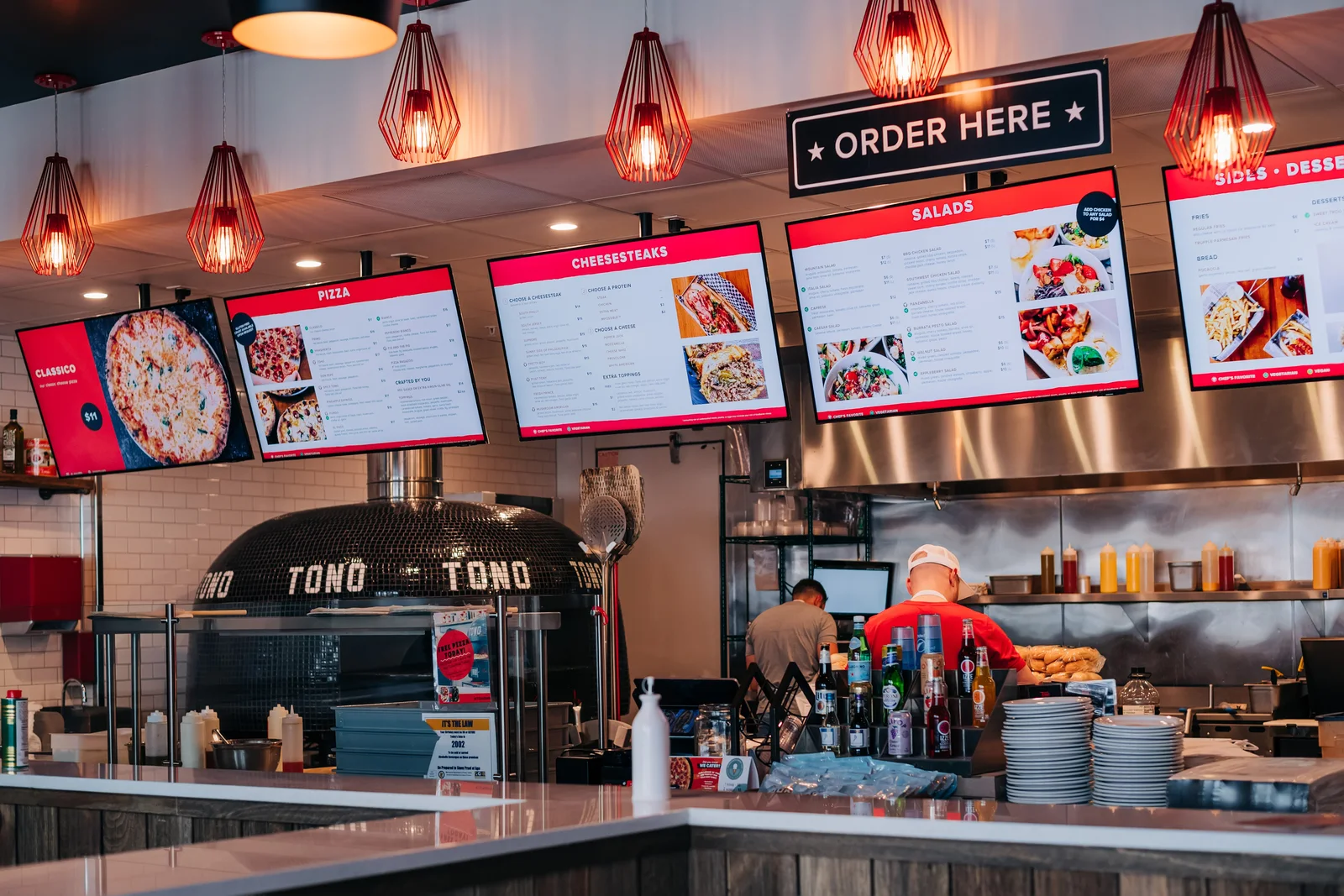Tono Pizzeria + Cheesesteaks service counter and open kitchen beneath red pendant lights in Chanhassen
