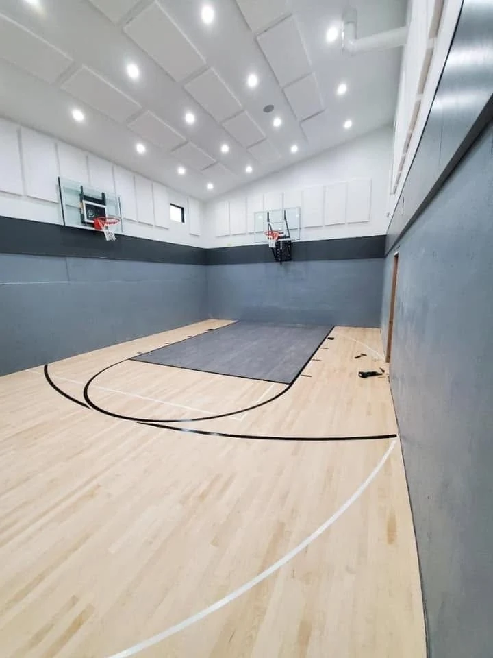 A completed indoor basketball court with wood flooring, gray walls and basketball hoops