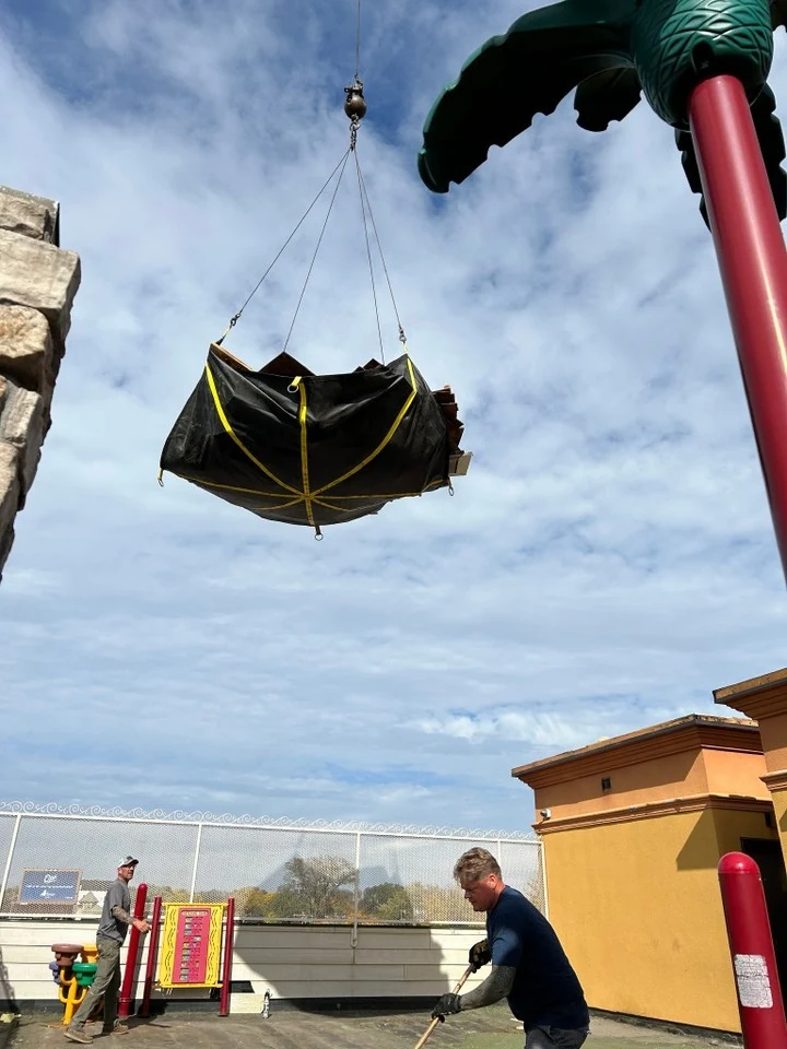 A crane lifts roofing debris above a school rooftop playground in Minneapolis